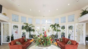 A spacious lobby with two red sofas facing a central round table surrounded by a floral arrangement. - Villa in Windsor Palms Resort 1260 (Kissimmee)