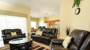 A living room with two leather sofas, a coffee table, and a dining area in the background. - Villa in Windsor Palms Resort 1260 (Kissimmee)