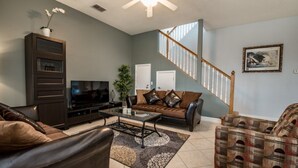 A living room with a sofa, a coffee table, a TV, a plant, and a staircase. - Orlando Villa for Rent With Gorgeous Pool, Vistapark Resort, Villa Orlando 1478 (Davenport)