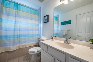A bathroom with a striped shower curtain, a toilet, a sink with a mirror, and a towel rack. - Orlando Villa for Rent With Gorgeous Pool, Vistapark Resort, Villa Orlando 1478 (Davenport)