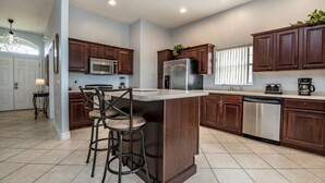 A modern kitchen with dark wooden cabinets, stainless steel appliances, and a central island with bar stools. - Orlando Villa for Rent With Gorgeous Pool, Vistapark Resort, Villa Orlando 1478 (Davenport)