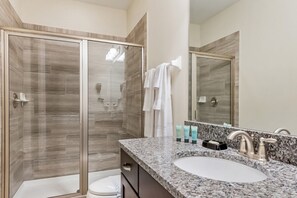 A modern bathroom with a glass-enclosed shower, a sink with a granite countertop, and a large mirror. - Villa in Encore Resort at Reunion 1952 (Kissimmee)