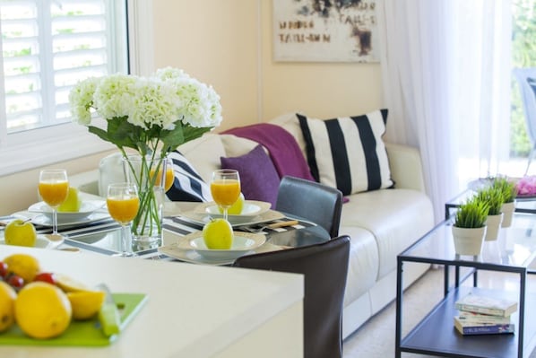 A modern living room with a sofa, a coffee table, and a dining area with a glass table set for breakfast.