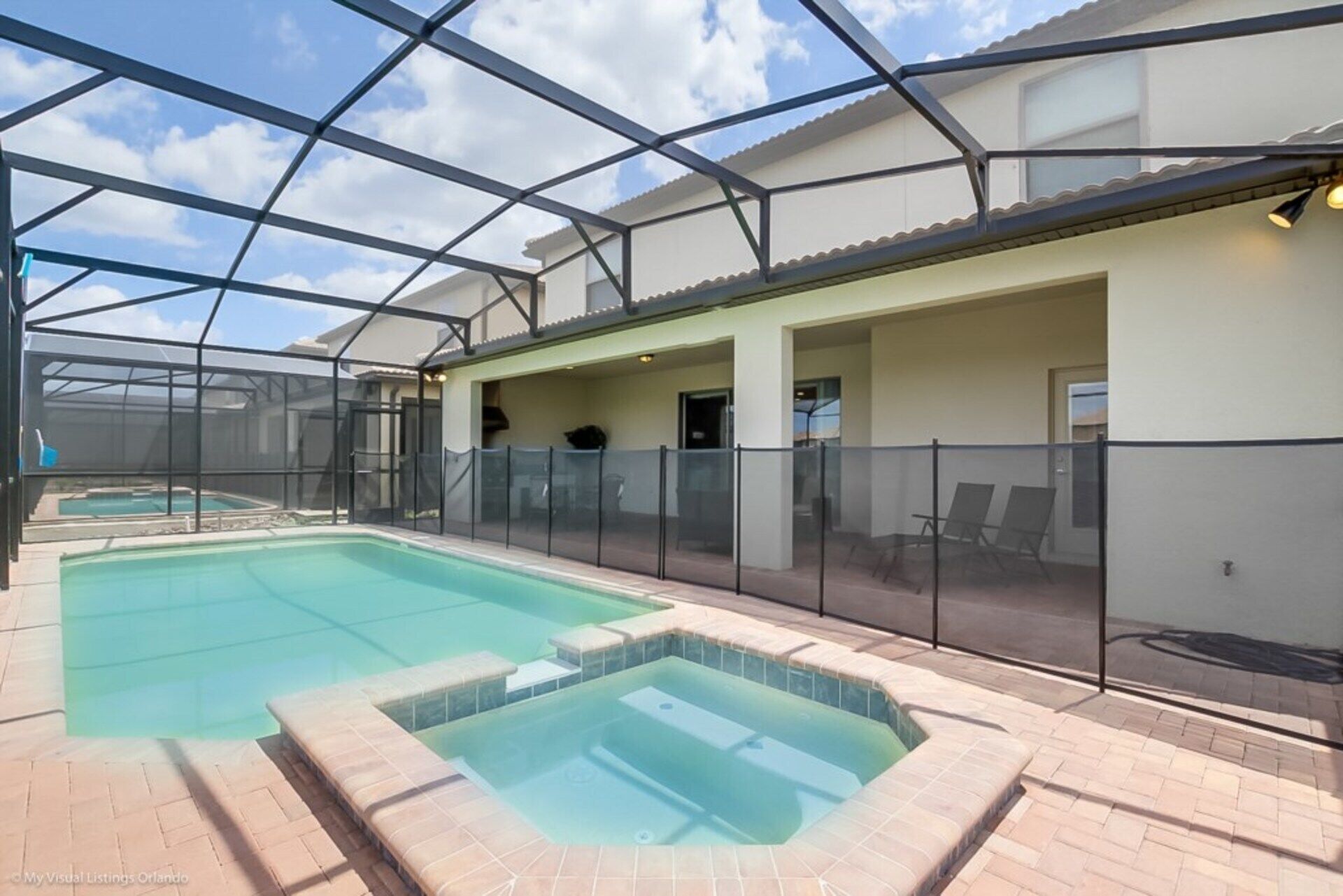A covered swimming pool area with a hot tub, lounge chairs, and a patio with a glass enclosure.