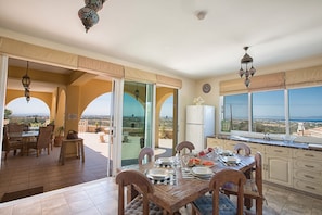 A spacious dining area with a view of the landscape, a kitchen with a large window, and a balcony with outdoor seating.