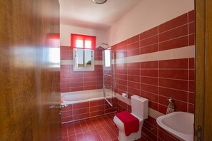A bathroom with red tiles, a white bathtub, a white toilet, and a white sink. - Villa for Rent in Protaras 1309 (Paralimni)