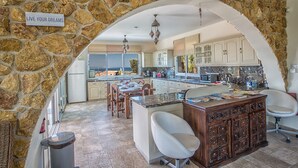 A spacious kitchen with a stone archway, a dining area with a large island, and a view of the outdoors. - Villa for Rent in Protaras 1309 (Paralimni)