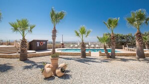 A pool area with palm trees, a lifebuoy, and a wooden structure. - Villa for Rent in Protaras 1309 (Paralimni)
