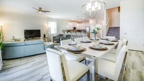A modern kitchen with white cabinets, a dining area with white chairs, and a large TV in the living room. - Villa in Champions Gate Resort 1751 (Davenport)