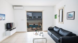 A modern living room with a black leather sofa, a coffee table, a TV, and a balcony with a dining table and chairs. - Luxury 3 Bedroom Villa With Private Pool, Paralimni Villa 1290 (Paralimni)