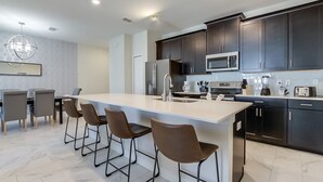 A modern kitchen with dark cabinets, a central island with bar stools, stainless steel appliances, and a large window. - Townhome in Champions Gate Resort 2544 (Davenport)