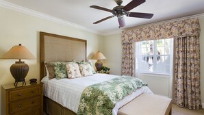 Un dormitorio con cama, dos lámparas de noche, una mesita de noche, cómoda y ventilador de techo, además de una ventana con cortinas.