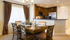 Comedor con mesa y sillas de madera, una araña y cocina con armarios de madera y electrodomésticos de acero inoxidable.