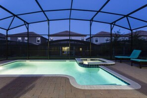 An outdoor swimming pool with a safety cover, surrounded by a brick patio and a view of houses in the background. - Villa in Champions Gate Resort 1136 (Davenport)