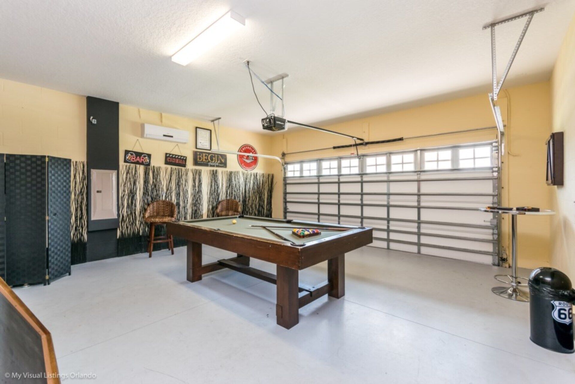 Une table de billard dans une pièce dotée d’une porte de garage, d’un porte-billes et d’une poubelle.