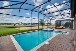 A covered swimming pool with a view of a grassy field and houses in the background. - Villa in Champions Gate Resort 2509 (Davenport)