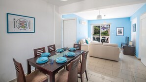 A dining area with a wooden table set for four, blue plates, and a white ceiling light. - Pernera Apartment 1207 (Paralimni)
