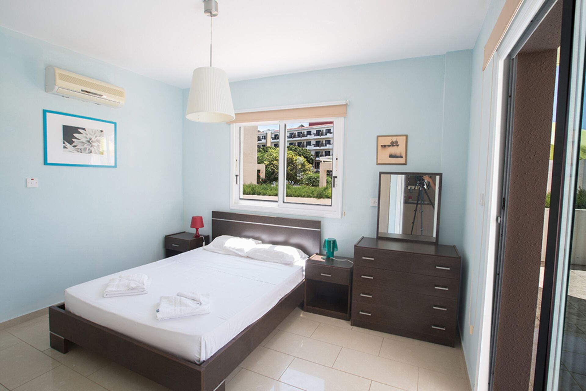 A bedroom with a bed, bedside tables, a dresser, a window with a view, and a ceiling fan.