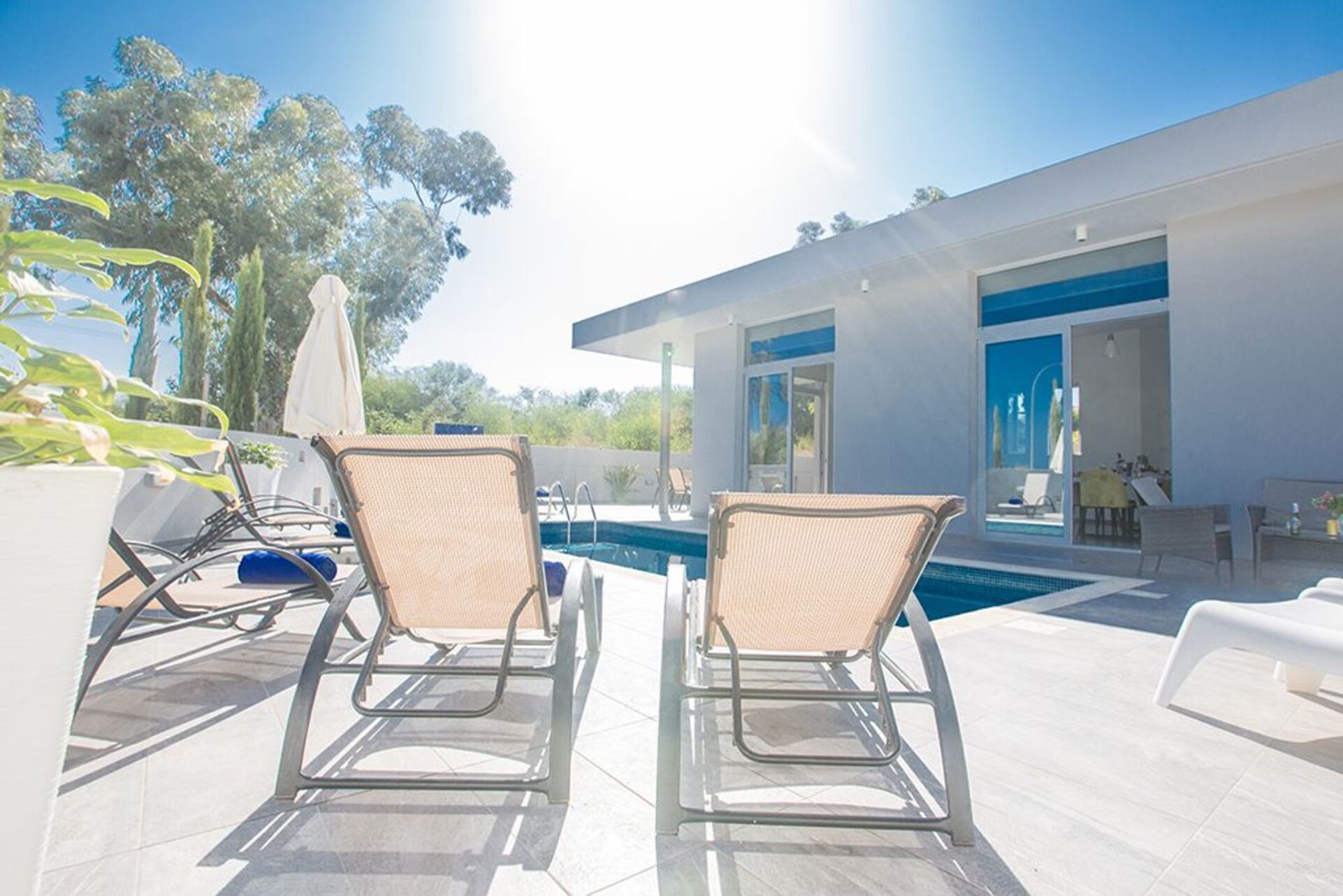 A modern house with a swimming pool, two lounge chairs, and a patio area.