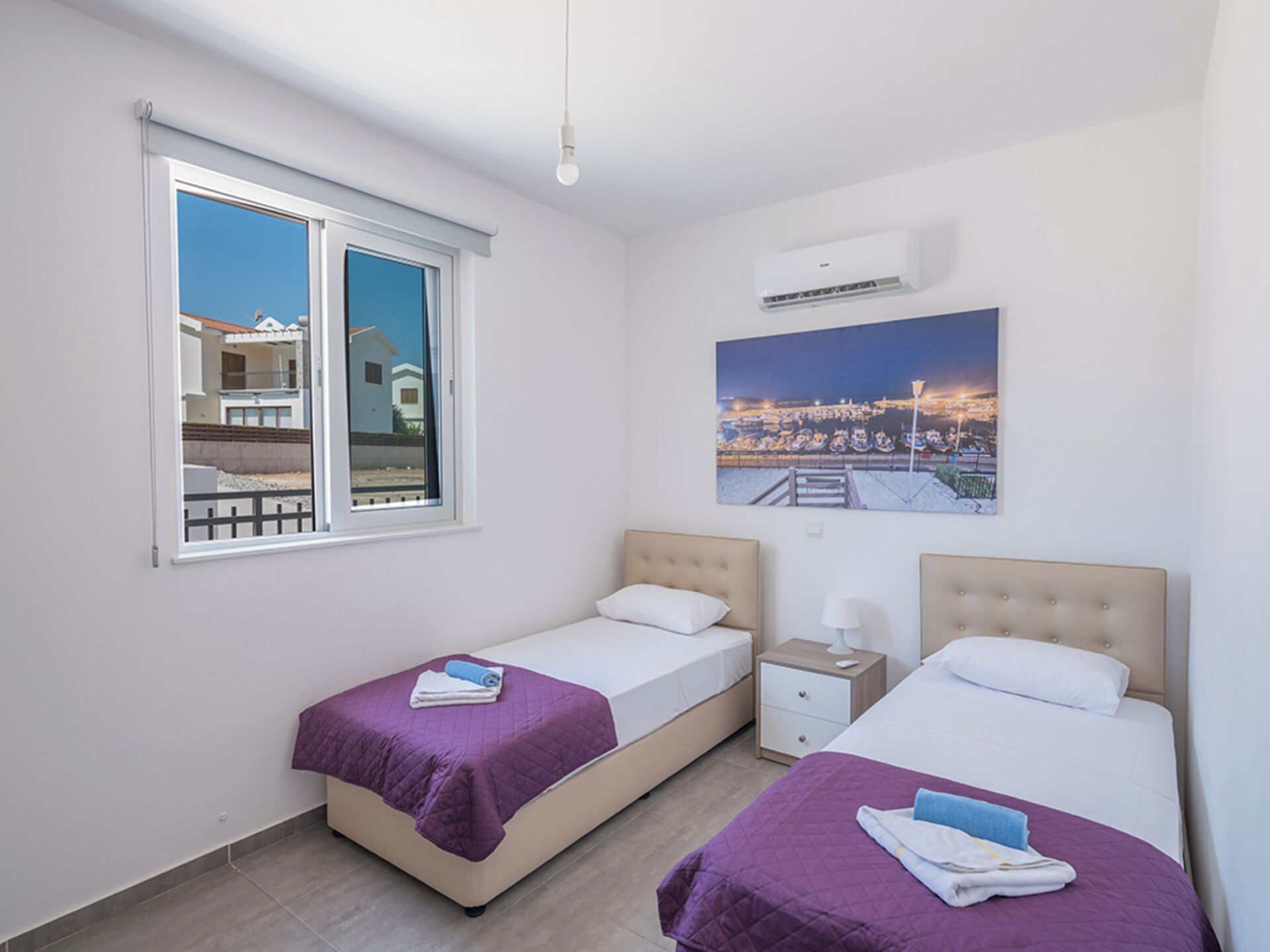 Une chambre d’hôtel avec deux lits, une fenêtre donnant sur des immeubles, un climatiseur et un tableau accroché au mur.