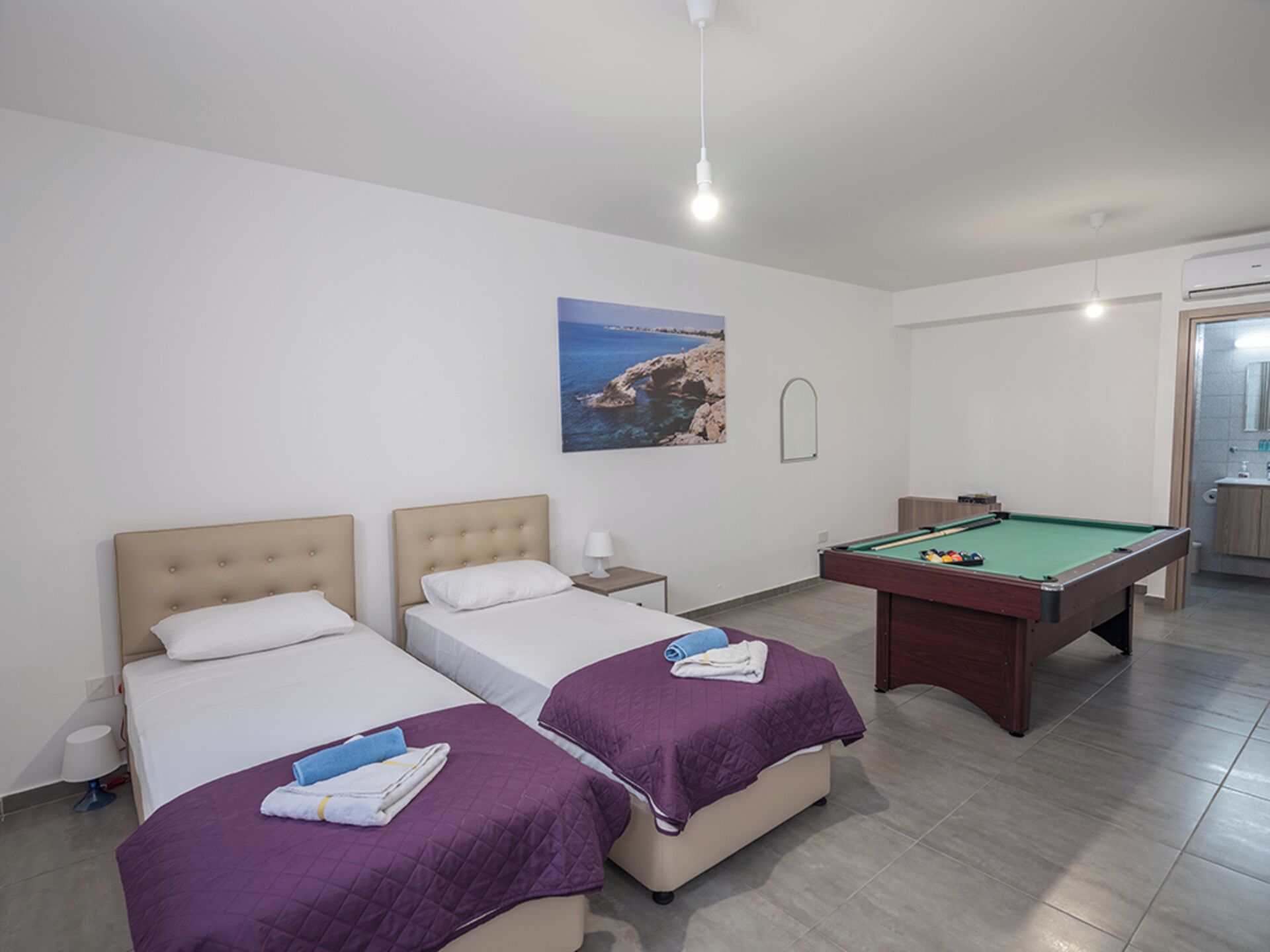 A hotel room with two beds, a pool table, and a painting of a coastal scene.