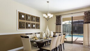 A dining area with a large table, chairs, and a chandelier. There are framed pictures on the wall and a view of a swimming pool through glass doors. - Private Resort Home 1131 (Davenport)