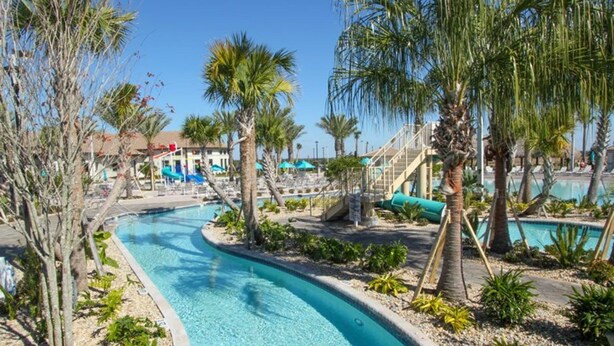 A pool area with a clear blue water feature, palm trees, and a building with a red roof in the background. - Private Resort Home 1131 (Davenport)