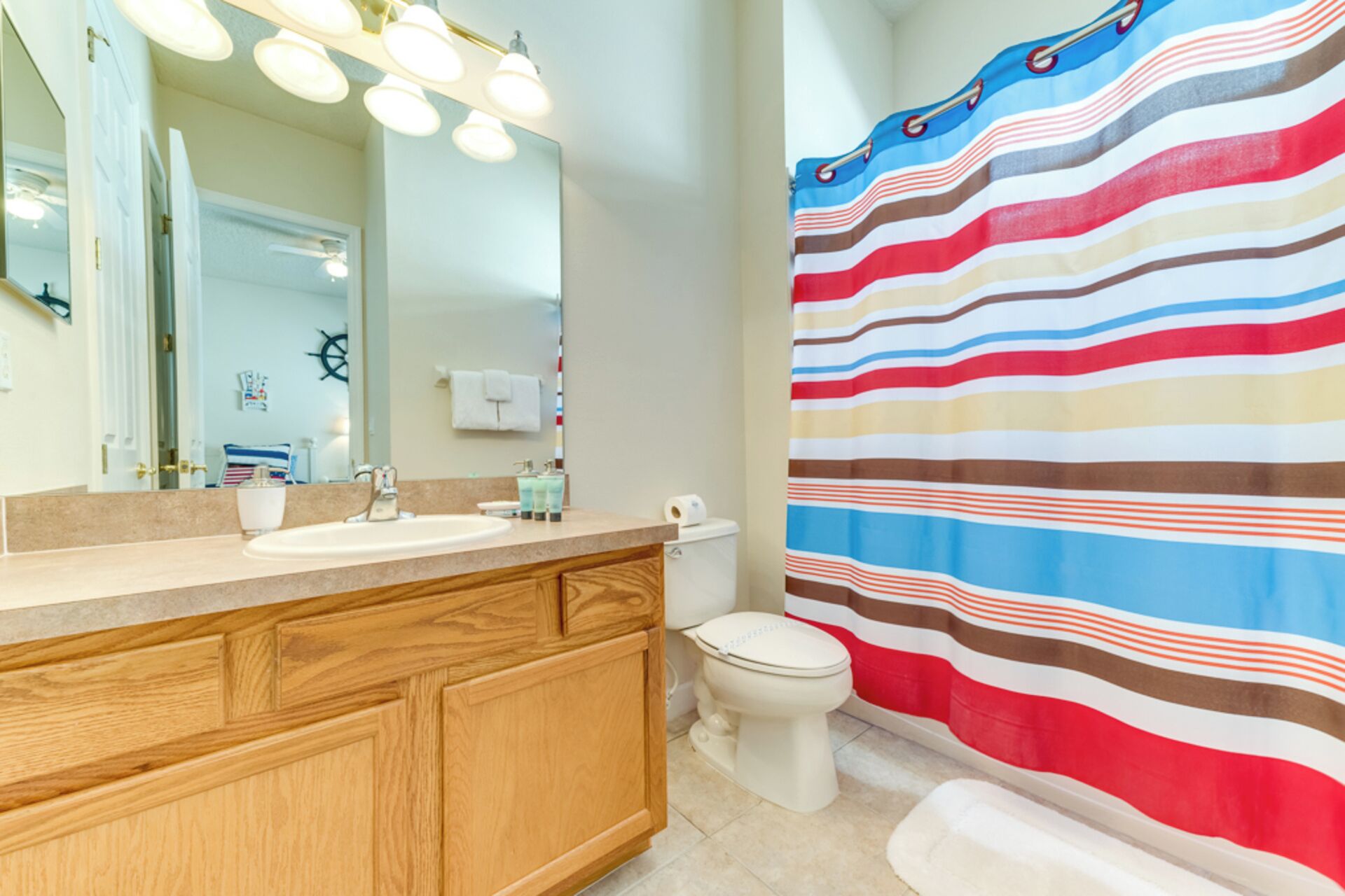 A bathroom with a wooden vanity, a sink, a mirror, and a striped shower curtain.