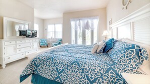 Un dormitorio con una cama grande, un aparador, un televisor y una ventana con cortinas.