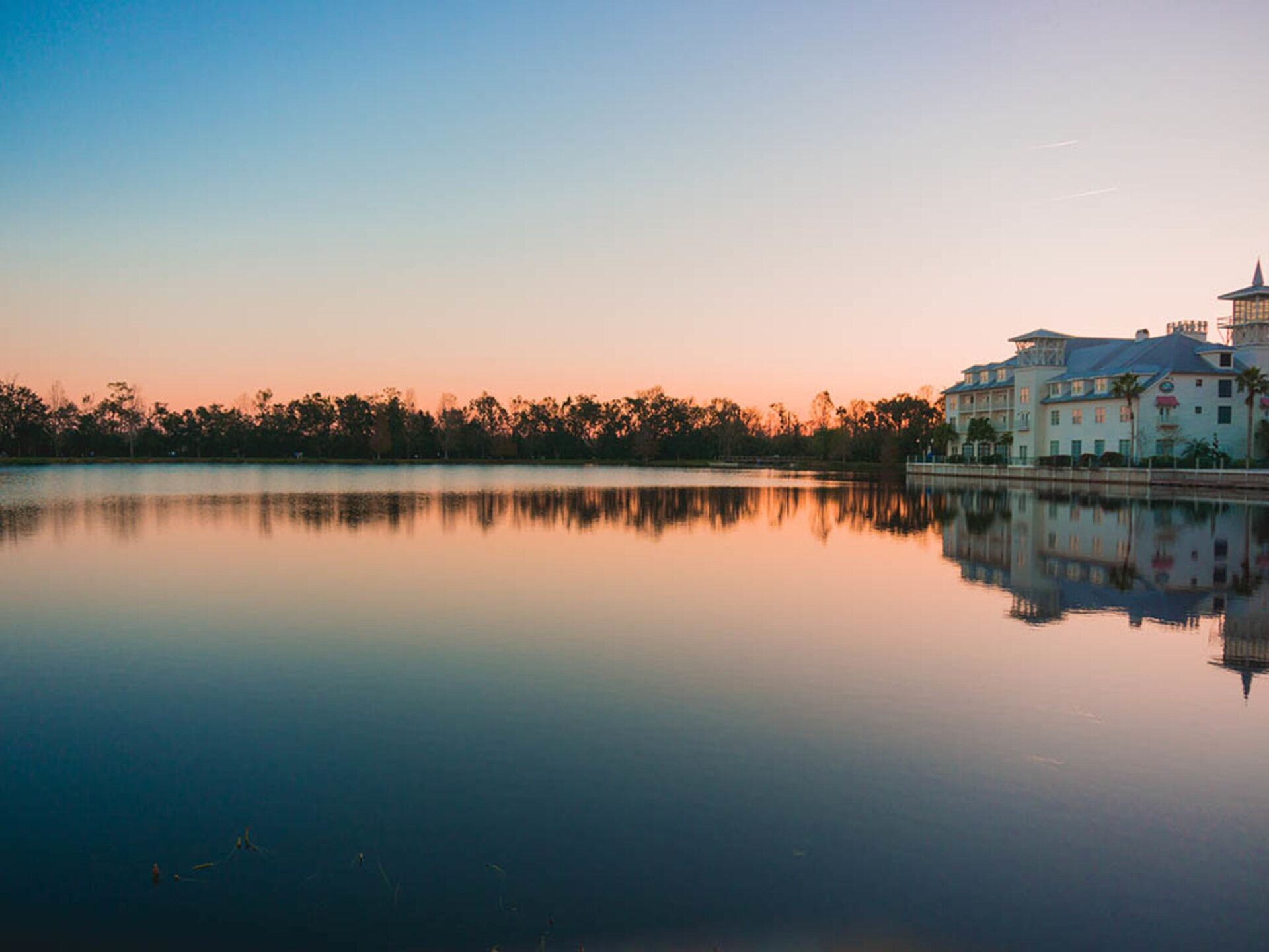 A calm lake with a reflection of a large building and trees.