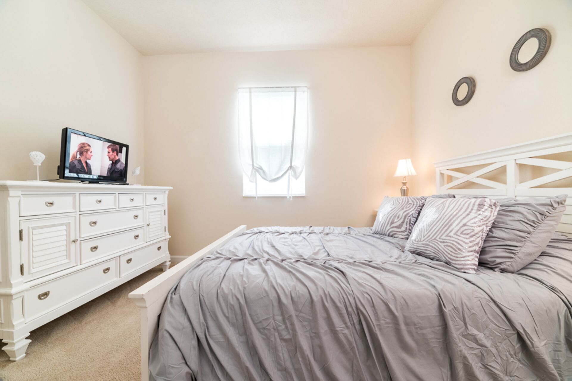 A bedroom with a bed, dresser, television, window, and wall decor.