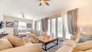 Amplia sala de estar con sofás color beige, una mesa de centro de madera y ventanas grandes con cortinas.