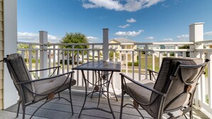 Un patio techado con dos sillas de metal y una mesa, con vistas a una zona residencial con casas y un cielo azul despejado.
