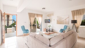 A spacious living room with a beige sofa, two blue armchairs, a coffee table, and a TV mounted on the wall. - Luxury Villa in Cyprus near Beach, Protaras Villa 1267 (Paralimni)