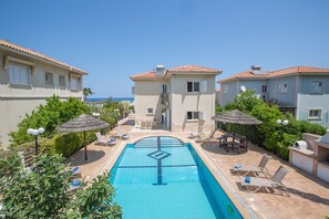 A pool area with lounge chairs and umbrellas, surrounded by buildings with tiled roofs. - Luxury Villa in Cyprus near Beach, Protaras Villa 1267 (Paralimni)