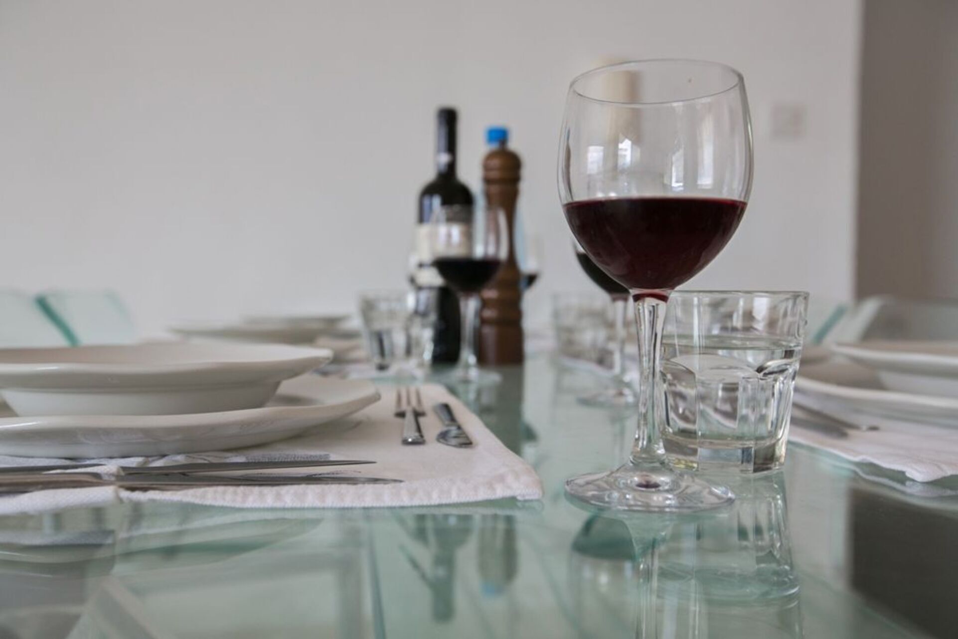 A dining table set with plates, cutlery, and a glass of red wine.