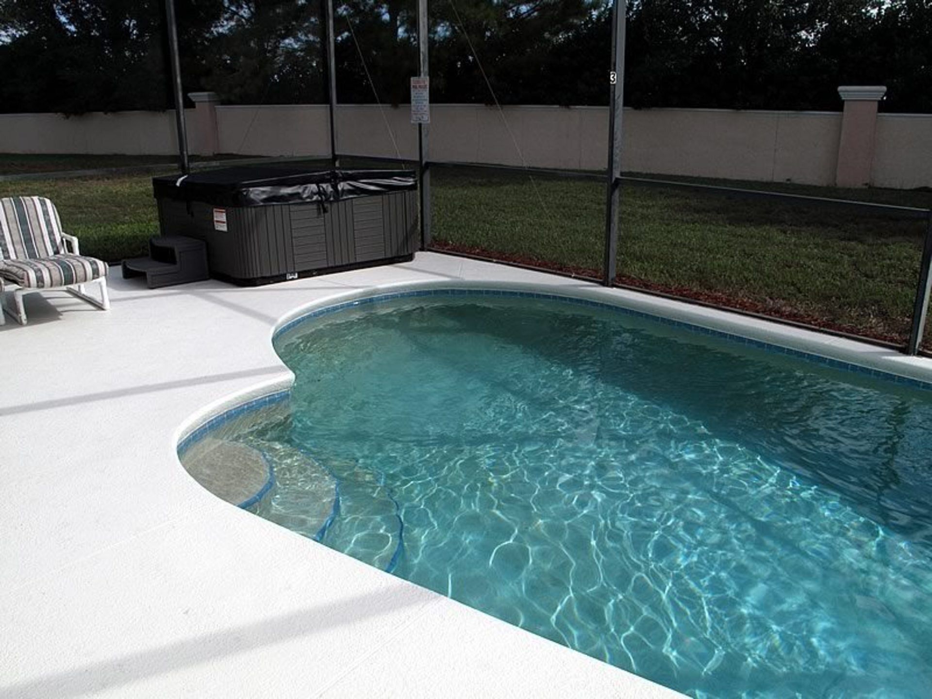 A swimming pool with a hot tub, surrounded by a white deck and a covered area.