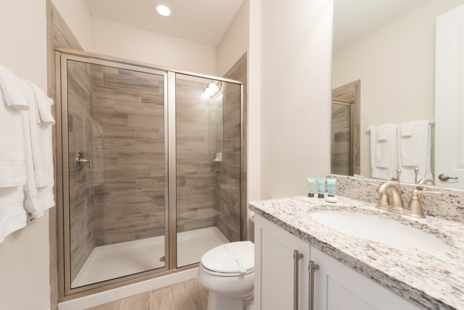 A modern bathroom with a glass-enclosed shower, a white toilet, and a marble sink with toiletries.