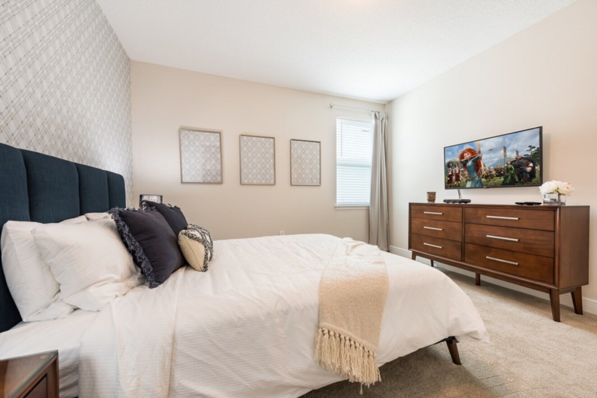 Quarto com cama, cômoda e televisão na parede.