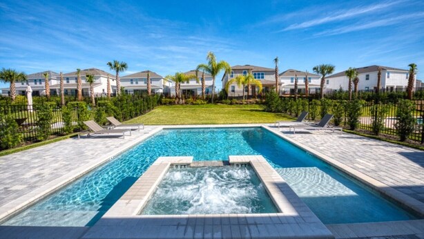 A swimming pool with a hot tub, surrounded by a well-maintained lawn and palm trees, with a row of houses in the background. - Villa in Encore Resort at Reunion 2979 (Kissimmee)