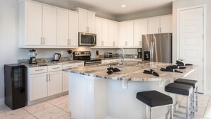 A modern kitchen with white cabinets, a large island with bar stools, stainless steel appliances, and a tiled floor. - Villa in Encore Resort at Reunion 2979 (Kissimmee)