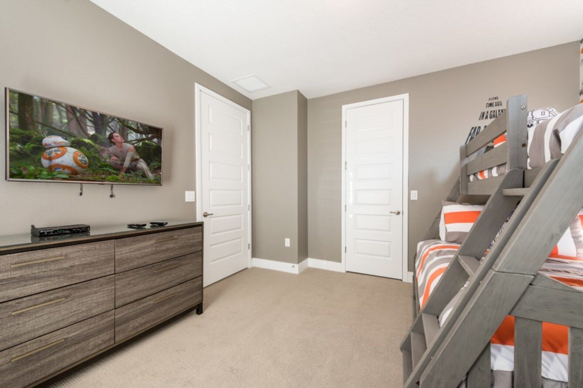 A bedroom with a bunk bed, a dresser, and a wall-mounted TV displaying a Star Wars scene.