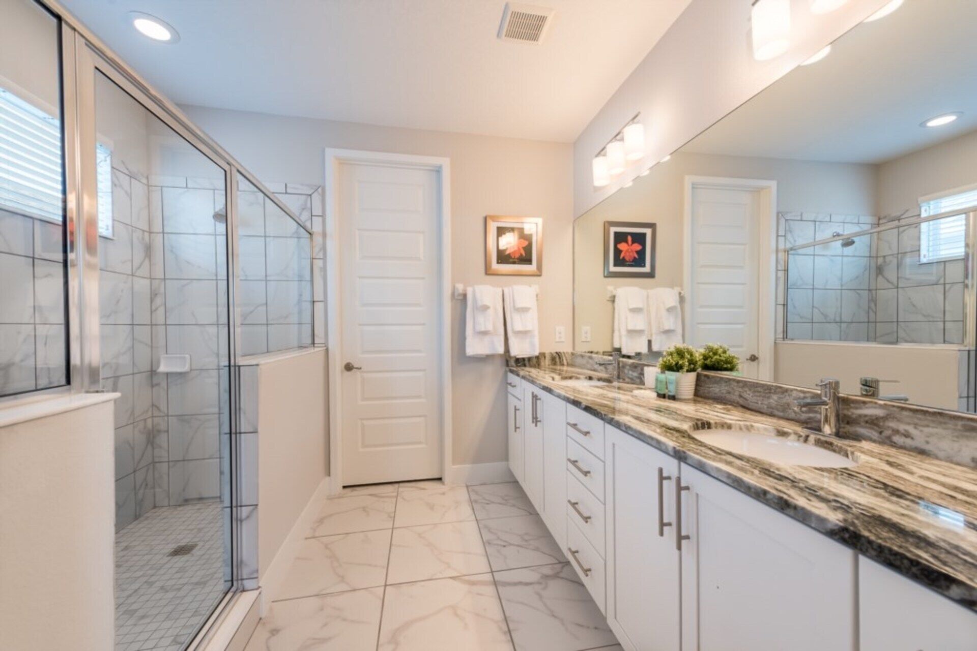 A modern bathroom with a glass shower enclosure, marble flooring, and a large mirror above the sink.