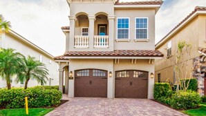 A two-story house with a balcony, two garage doors, and a brick driveway. - Luxury Villa With Majestic Golf Course Views, Reunion Resort, Villa Orlando 1795 (Kissimmee)