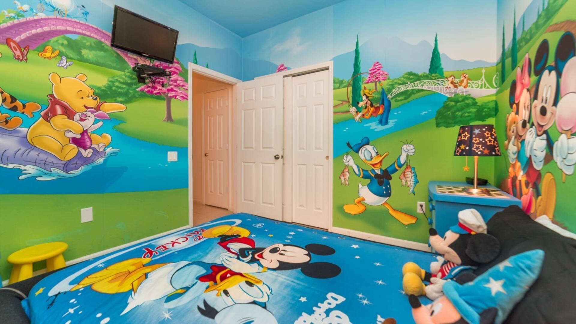 Ein Kinderzimmer mit Wandmalereien zum Thema Disney, einem Bett mit Mickey Mouse Bettwäsche und einem an der Wand montierten Fernseher.