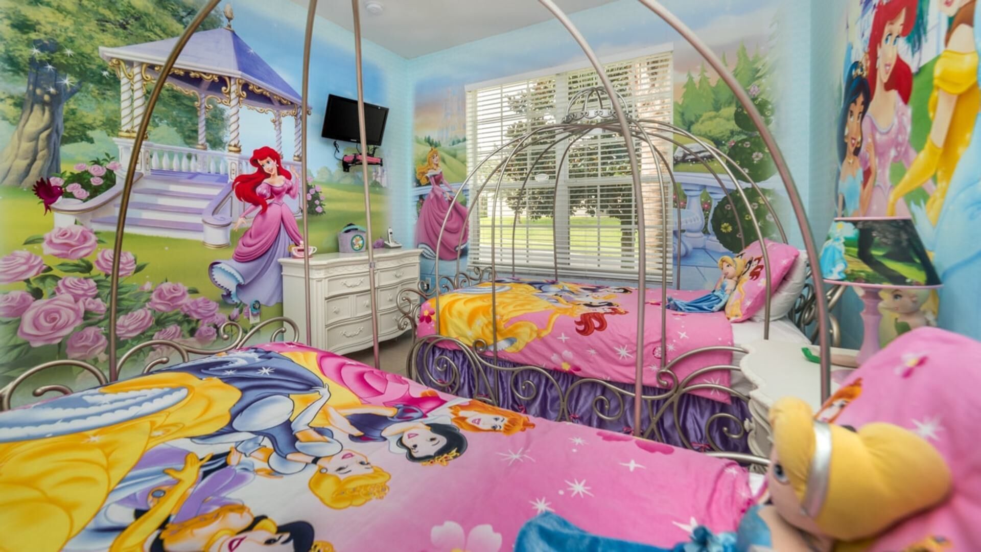 A bedroom with a canopy bed, a dresser, a vanity, and a TV mounted on the wall.