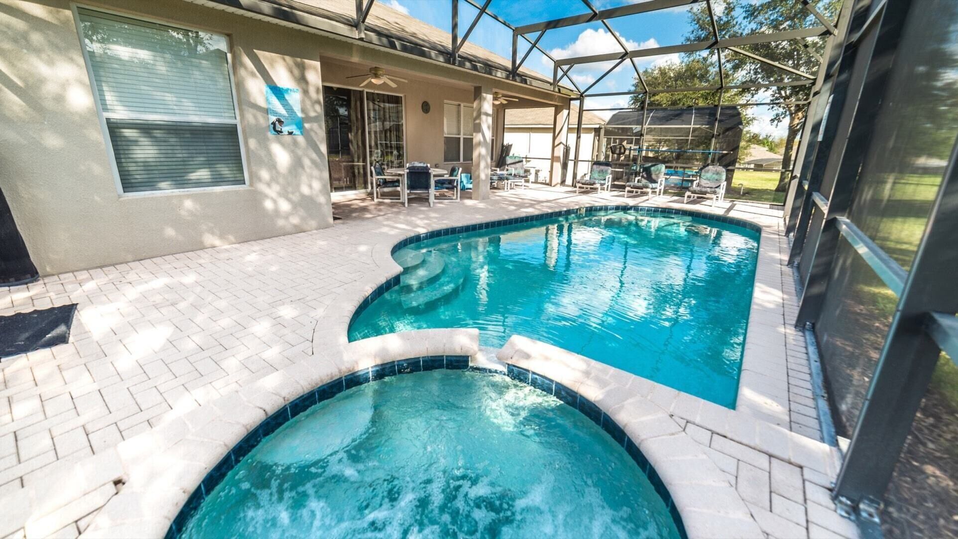 A swimming pool with a hot tub, surrounded by a covered patio area with chairs and a table.