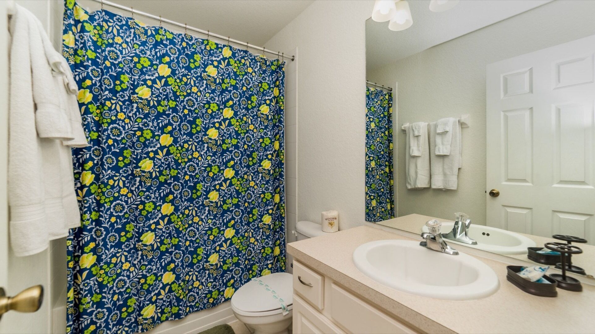 A bathroom with a floral shower curtain, a white toilet, a sink with a mirror, and a towel rack.