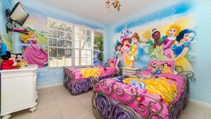 Camera per bambini con due letti, una finestra con persiane, un comò e un affresco raffigurante le principesse Disney.