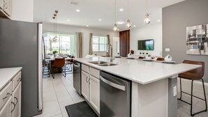 A modern kitchen with a central island, stainless steel appliances, and pendant lighting. - Villa in Solterra Resort 2764 (Davenport)